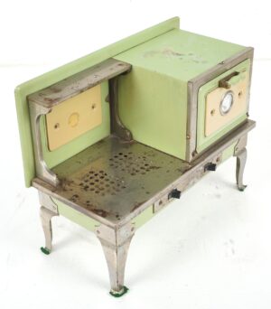 Vintage toy stove in pale green and cream enamel with four nickel-plated legs, shown in a three-quarter view with surface wear and chipped paint.