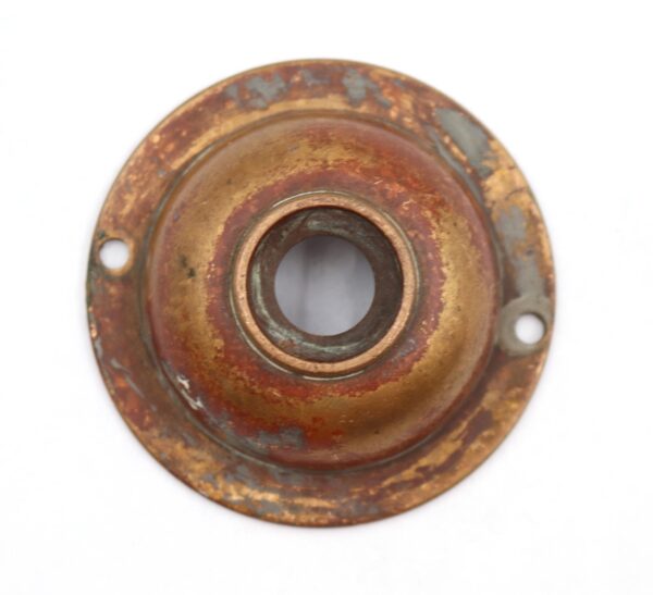 Vintage circular brass doorbell cover with two mounting holes and a center opening, shown in a close-up view with visible surface wear and patina finish.