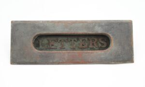 Vintage bronze mail slot cover plate with a spring-loaded opening and visible wear, shown with the word letters cutout inside.