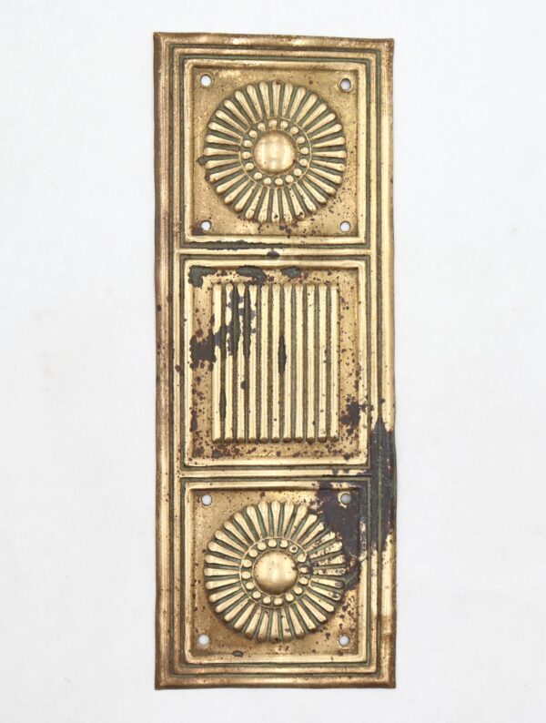 Pressed brass door push plate with top and bottom sunburst rosettes and a central reeded column, shown vertically with heavy surface wear and oxidation.