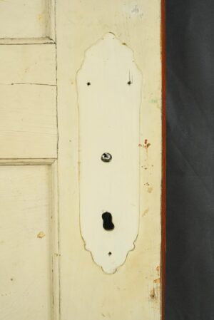 Close-up of a vintage wood door showing a decorative trim plate with keyhole and screw holes, plus worn painted surface details.