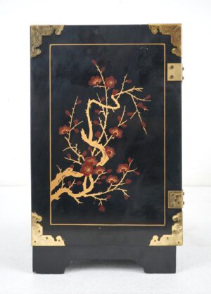 Front view of a black lacquer cabinet with hand-painted floral branches, polished brass corner guards, and strap hinges.