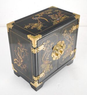 Black lacquer cabinet with hand-painted nature motifs, polished brass corner guards, strap hinges, and a central medallion with round pulls.