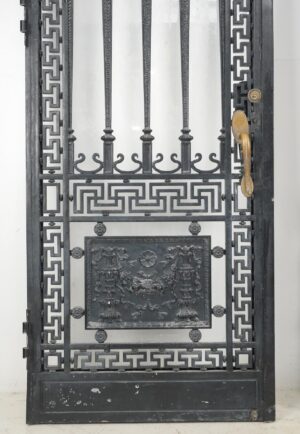 French wrought iron entry door with Greek key frame, ornate relief panel, and original brass pull visible on one side.