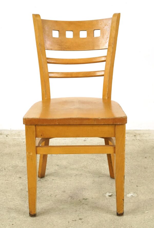 Light wood tone chair with a curved backrest, four square cutouts, and horizontal slats below, shown front on with visible surface wear.