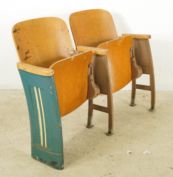 Three vintage theater seats with molded plywood backs, flip-up seats, and cast iron frames, shown in a row with visible wear and a green end panel.