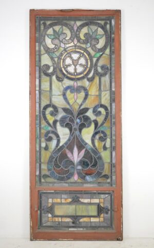 Rectangular leaded stained glass church window with a terra cotta painted wood frame and multicolored panels, shown full length with decorative scrollwork and a smaller framed section below.