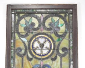 Rectangular stained glass church window with a reddish-orange wood frame, showing a central circular floral pattern in yellow, blue, green, and pink glass.