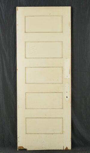 Vintage swinging wood door with five horizontal panels, painted white with visible surface wear and a handle cutout on the right side.
