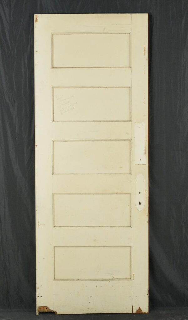 Vintage swinging wood door with five horizontal panels, painted white with visible surface wear and a handle cutout on the right side.