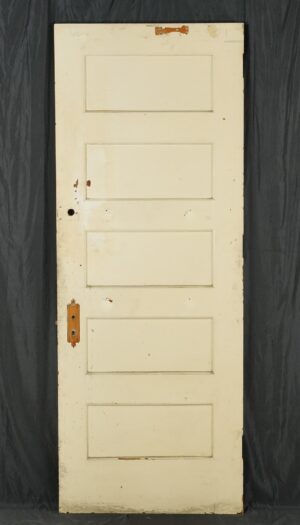 Vintage five-panel wood door painted white, shown with the original brass lock hardware and visible surface wear.