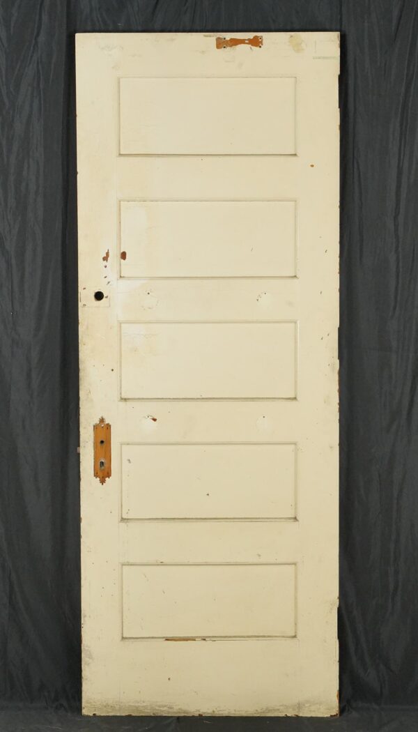Vintage five-panel wood door painted white, shown with the original brass lock hardware and visible surface wear.