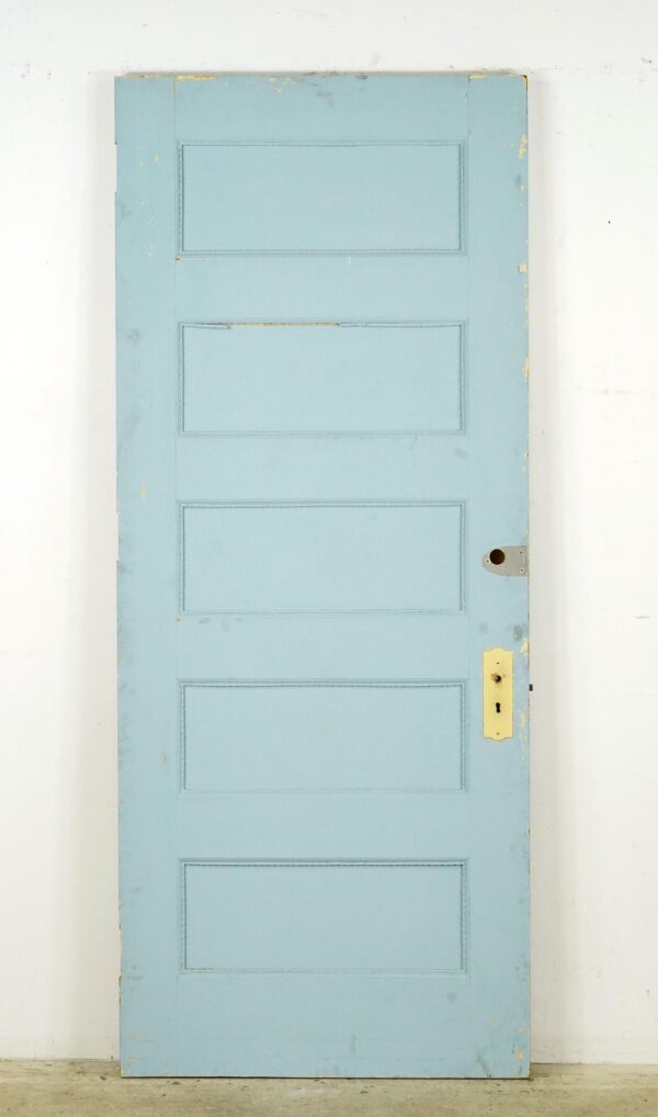 Vintage five-panel privacy door painted blue with an antique brass lock on the right side and visible surface wear.
