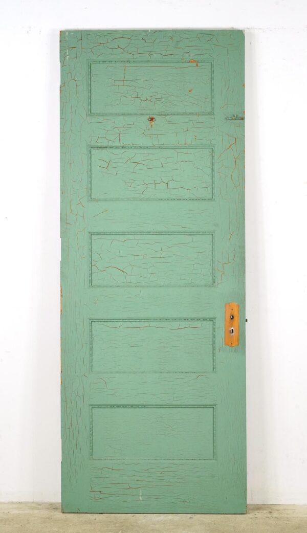 Vintage five-panel passage door with cracked green paint, decorative trim, and an attached brass lock plate visible on the right side.