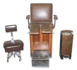1930s doctor’s equipment set showing an examination chair with slide-out footrest and side cabinet, a swivel stool, and a pushbin waste bin.