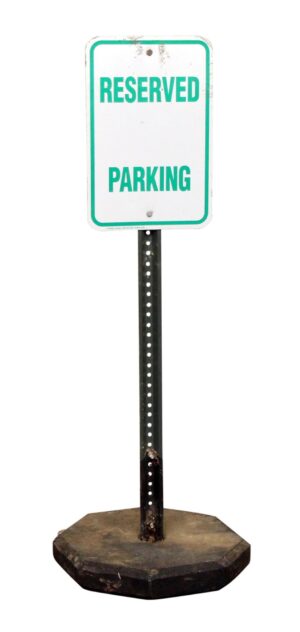 Free-standing reserved parking sign with a green and white face on a black post and weighted base, shown full length with visible surface wear.