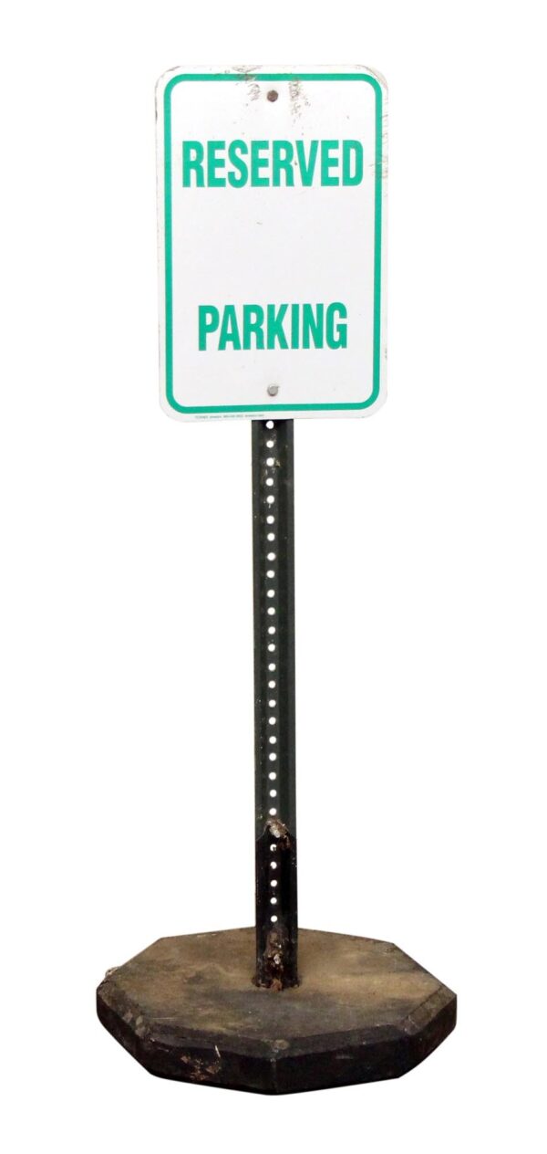 Free-standing reserved parking sign with a green and white face on a black post and weighted base, shown full length with visible surface wear.