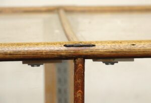 Close-up of an antique retail showcase showing the oak frame with clear glass and added support pieces, viewed from the side in a restored section.