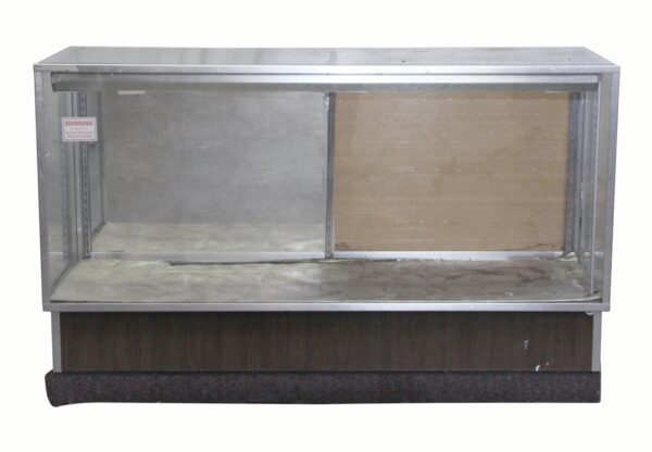 Glass-walled showcase with a brushed aluminum frame, sliding back doors, and a dark wood-tone base, shown from the front with visible wear.