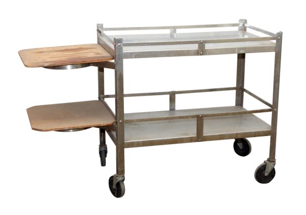 Two-tier steel hospital utility cart with light wood side shelves and caster wheels, shown in three-quarter view with visible surface wear.