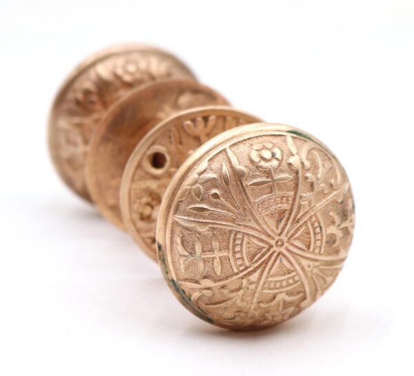 Close-up of a polished brass door knob with an embossed floral pattern and a matching knob partially visible behind it.