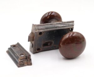 Antique door knob set with two brown ceramic knobs, a cast iron rim lock, and a catch shown in a close-up view.