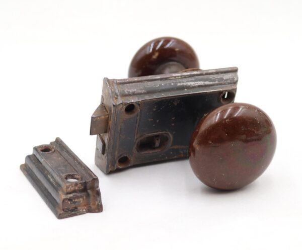 Antique door knob set with two brown ceramic knobs, a cast iron rim lock, and a catch shown in a close-up view.