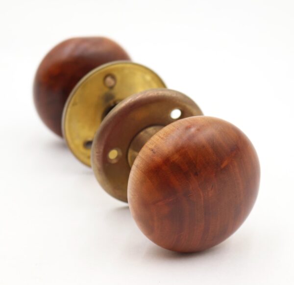Antique passage door knob set with two dark wood knobs, brass rosettes, and spindle shown in a close-up view.
