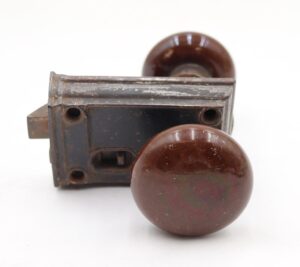 Brown ceramic door knob set with a cast iron rim lock, shown in close-up with visible surface wear and rust.