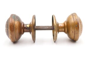 Antique brass passage door knob set with two knobs, two rosettes, and a spindle shown in side view, featuring heavy surface wear and visible decorative detailing.
