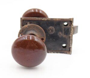 Brown ceramic door knob set with a cast iron rim lock, shown in close-up with surface wear and rust.