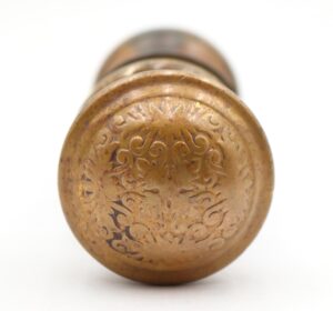 Antique brass door knob shown in close-up, with an engraved floral pattern and visible surface wear on the round face.
