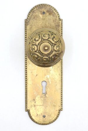 Victorian brass dummy door knob set with a beaded back plate, a round ornate knob, and a keyhole opening visible on the rectangular plate.