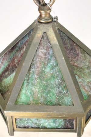 Hexagonal pendant light with brass framing and marbled green slag glass panels, shown from above with the top finial and chain attachment visible.