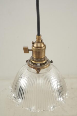Close-up of a pendant light with a ribbed clear glass shade, antique brass fitter, and black cord.