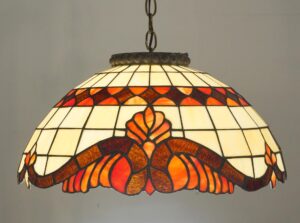 Tiffany-style stained glass pendant light with cream, amber, and orange floral geometric panels and an antique brass canopy.