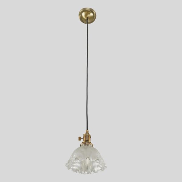 Industrial pendant light with a clear Holophane-style glass shade, black cord, and antique brass fitter.