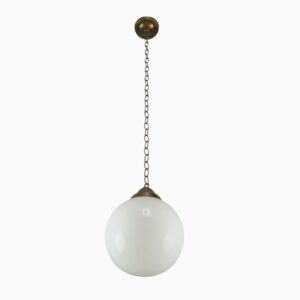 Schoolhouse pendant light with a round white glass globe and antique brass chain canopy.