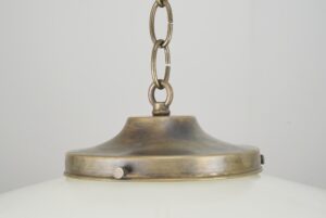 Art Deco pendant light with a milk glass globe and antique brass chain fitter shown in a close-up of the top and chain connection.