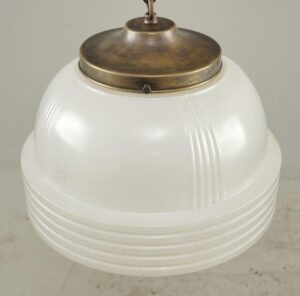 Art Deco pendant light with a white Fresnel lens globe and antique brass fitter, shown in a close-up view.