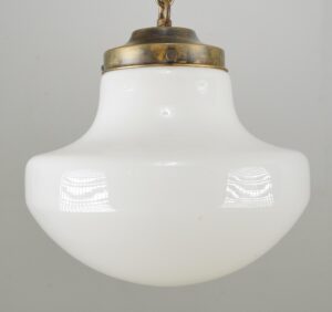 Schoolhouse pendant light with a white milk glass globe and antique brass chain fitter, shown in a close-up view.