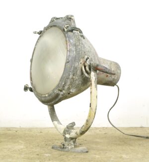 Vintage industrial ship spotlight with a thick round glass lens, adjustable mounting arm, and visible surface wear, shown in a side view.