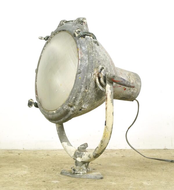 Vintage industrial ship spotlight with a thick round glass lens, adjustable mounting arm, and visible surface wear, shown in a side view.