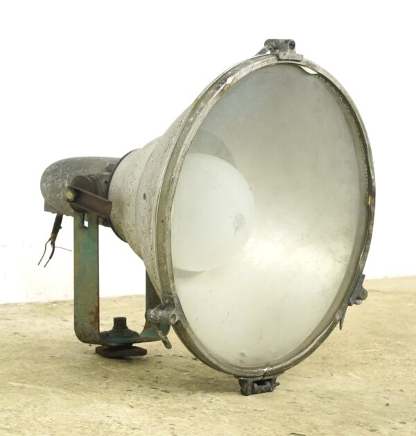 Vintage industrial floodlight with a large curved glass lens, green housing, and visible mounting hardware shown in side view with surface wear.