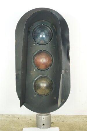 Vintage vertical railroad signal light with three stacked glass lenses and a curved metal hood.