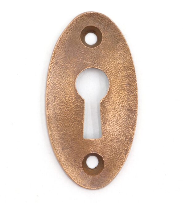 Vintage brass oval keyhole cover plate with a textured surface and centered keyhole opening, shown front view with two screw holes.