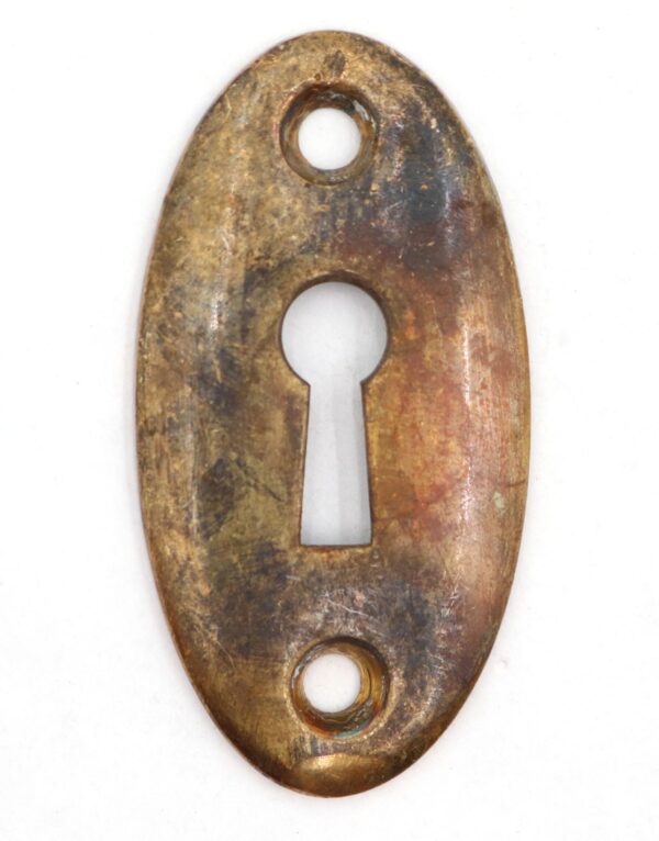 Vintage brass oval keyhole cover plate with an antique finish and a central keyhole opening, shown front view with two mounting holes.