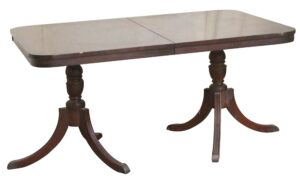 Regency Revival drop-leaf dining table in dark wood tones with two tripod pedestal bases and a rectangular top showing a center seam and slight surface wear.