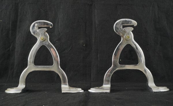 Pair of chrome butcher rack hook brackets shown side by side, with curved mounting feet and worn surface finish visible on each piece.