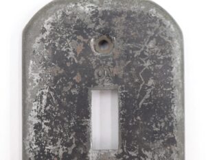 Distressed black steel toggle switch cover wall plate with a single toggle opening and centered screw hole, shown in a close-up front view.